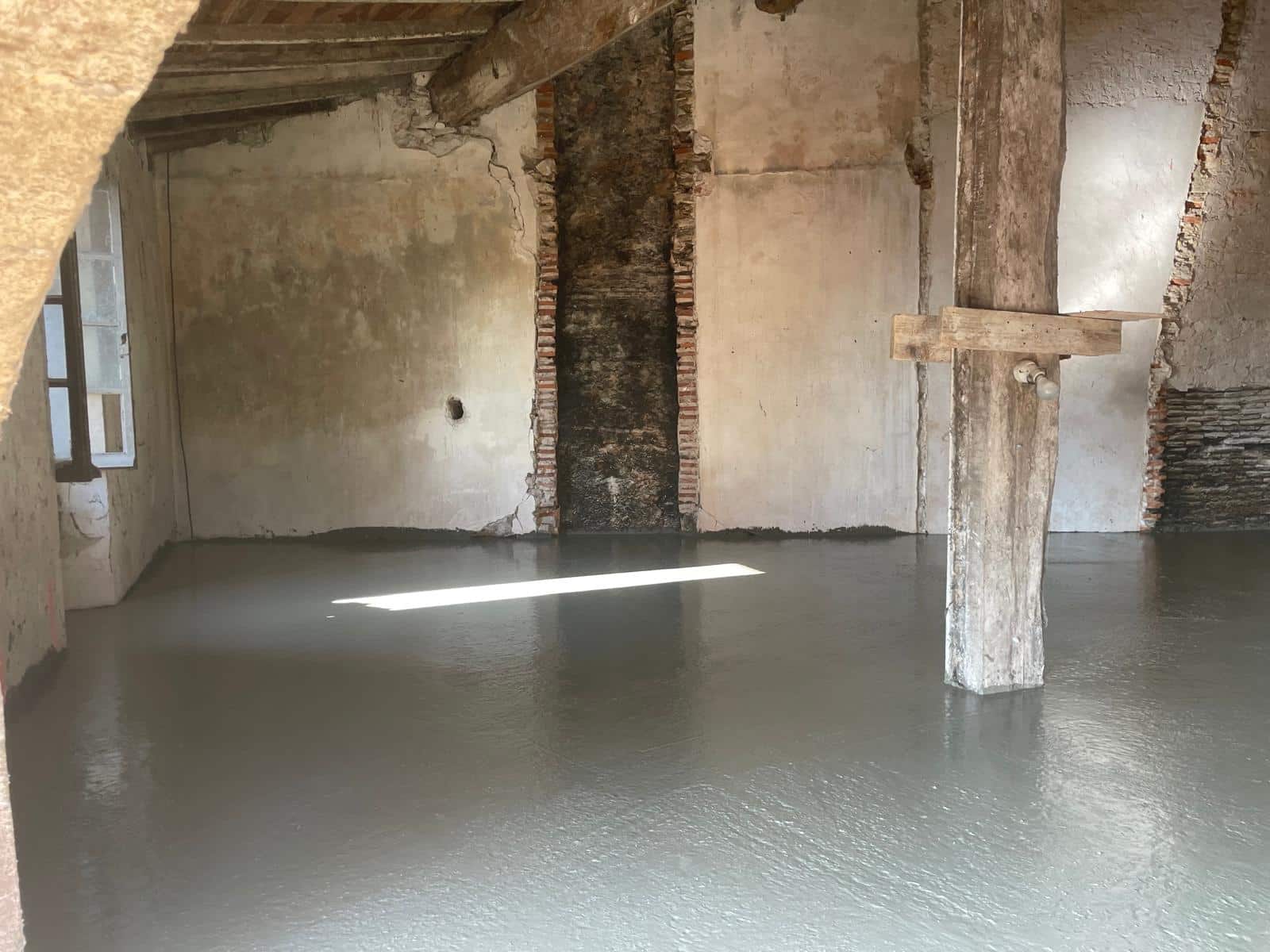 Réalisation d’une dalle béton neuve dans une bâtisse ancienne en rénovation avec reprise des murs en pierre et conservation des poutres bois apparentes